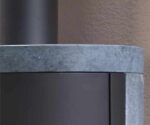 De afbeelding toont een detail van het bovenste gedeelte van een houtkachel. Te zien is een elegant, afgerond oppervlak van steen, dat de houtkachel een moderne en stijlvolle uitstraling geeft. Dit detailbeeld benadrukt de hoogwaardige afwerking en het aantrekkelijke ontwerp van de houtkachel. Ideaal voor wie op zoek is naar een efficiënte en esthetisch aantrekkelijke houtkachel.