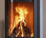 De afbeelding toont een gedetailleerd detail van een houtkachel, waarbij vooral de kijkruit wordt benadrukt. Achter de gebogen ruit zijn levendige vlammen en brandend hout te zien, wat een warme en uitnodigende sfeer creëert. Door de focus op de ruit komen de structuur en de helderheid van het zicht duidelijk tot hun recht, wat de aantrekkelijkheid van de houtkachel onderstreept. Ideaal voor een gezellige avond voor de houtkachel.