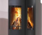 De afbeelding toont een moderne houtkachel met de nadruk op de glazen zijkant, die uitzicht biedt op het levendige vlammenspel binnenin. De kachel heeft een elegant, zwart ontwerp en biedt dankzij het royale kijkvenster een sfeervol uitzicht op het vuur. Dit detailbeeld onderstreept de hoogwaardige afwerking en de stijlvolle integratie in elke woonruimte. Houtkachel, glazen voorkant, houtkachel.