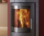 Alt-Text: Detailansicht eines stilvollen Kaminofens mit Fokus auf der Frontscheibe. Die Scheibe ermöglicht einen klaren Blick auf die lebendig flackernden Flammen im Inneren, was eine gemütliche Atmosphäre schafft. Der elegante Metallrahmen rundet das moderne Design ab und betont die hochwertige Verarbeitung des Holzofens. Perfekt zur Ergänzung moderner Wohnräume.