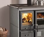 Das Bild zeigt einen Ausschnitt eines Kaminofens mit dem Fokus auf der Brennkammer. Die Flammen sind durch die Glasscheibe deutlich sichtbar, was eine gemütliche und einladende Atmosphäre vermittelt. Der Ofen hat eine robuste, moderne Optik und scheint aus hochwertigen Materialien gefertigt zu sein. Ideal für jedes Zuhause, das Wärme und Stil kombinieren möchte. Perfekt geeignet für SEO, sind die Keywords Kaminofen und Holzofen.