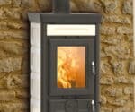 Sofia Evo-brændeovn med beige Maiolica-beklædning, ilden brænder bag glasruden foran en stenmur.