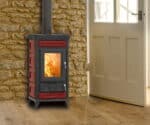 Rød Sofia Evo Maiolica-brændeovn foran en stenmur med synlig ild gennem glasdøren.