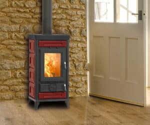 Rød Sofia Evo Maiolica-brændeovn foran en stenmur med synlig ild gennem glasdøren.
