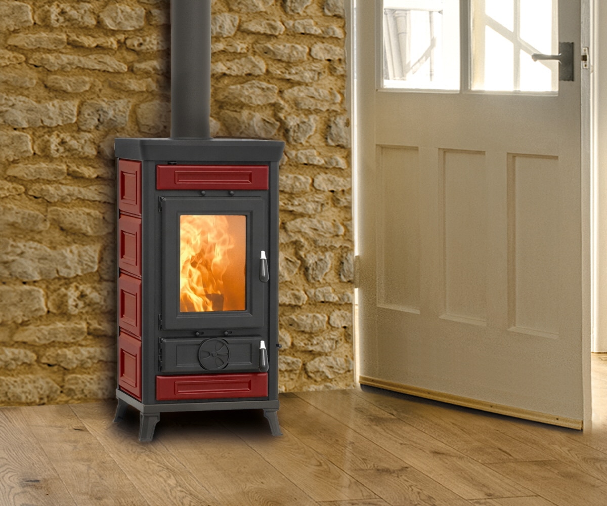 Sofia_Evo_Maiolica_rood Rode Sofia Evo Maiolica houtkachel voor een stenen muur, met zichtbaar vuur door de glazen deur.