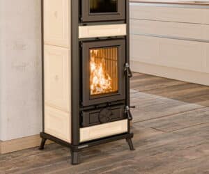 Beige brændeovn med brændende ild, rektangulær glasfront, moderne køkken i baggrunden.