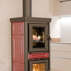 Rode houtkachel met stalen pijp, twee deuren, bovenste deur met kijkvenster naar de oven, onderste deur met vlammen.