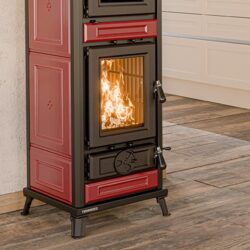 Rode Agnese Maiolica kachel met brandend vuur achter glas, staat op houten vloer voor witte muur.