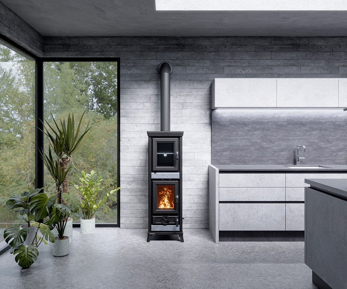 agnese_stone-3_1920x1080 Moderne brændeovn i et lyst betonkøkken ved siden af store planter og høje vinduer, der lukker masser af lys ind.