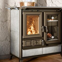 Kachel met brandend vuur achter glazen ruit, focus links. Kachel met thermometer en braadstuk rechts.