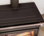 Detailed view of a wood-burning stove with a black surface and a handle. The flame image can be seen in the background.