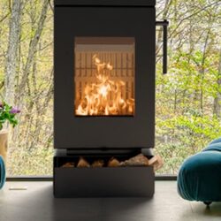 Close-up of a modern wood-burning stove with flames inside, surrounded by green plants and blue cushions.
