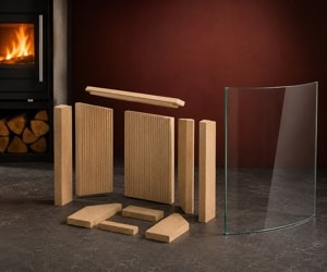 Stove accessory with fireclay bricks and curved glass pane, arranged on a dark floor. A burning fireplace in the background.