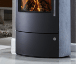 Detailansicht eines Kaminofens mit brennendem Feuer hinter einer Sichtscheibe. Der Ofen hat eine glatte, dunkle Oberfläche und seitliche Specksteinverkleidung.